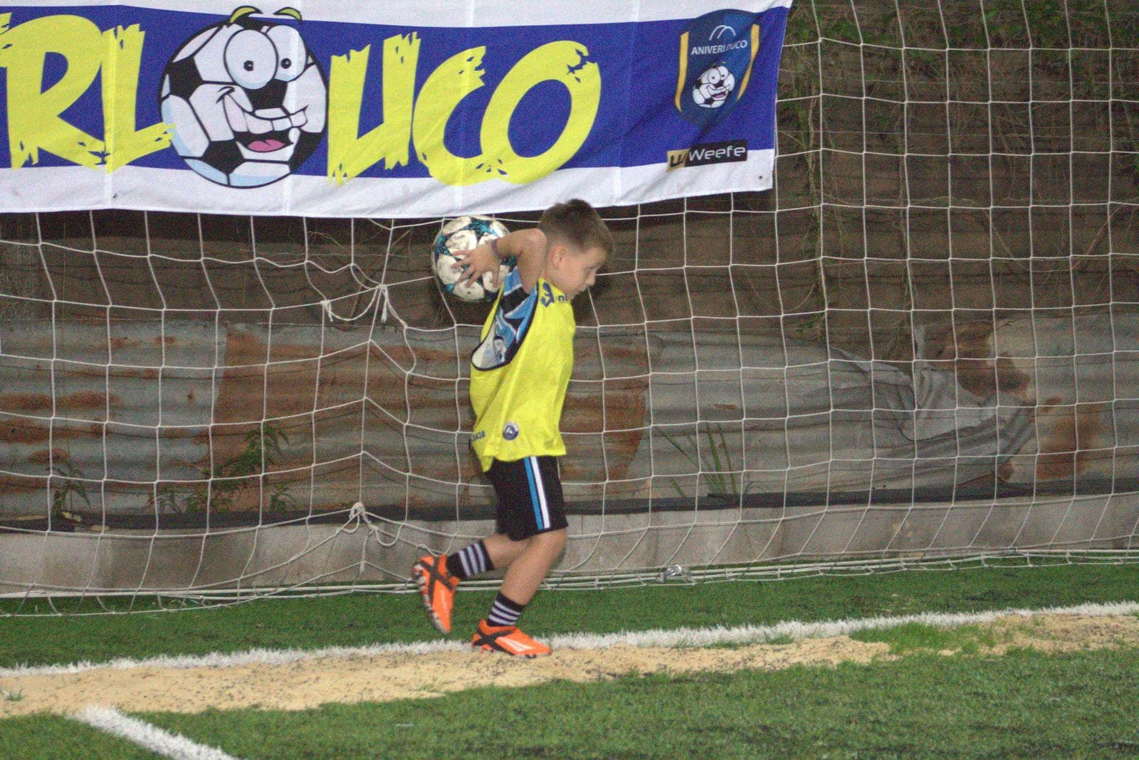 Criança com a bola em frente ao banner do Aniverlouco